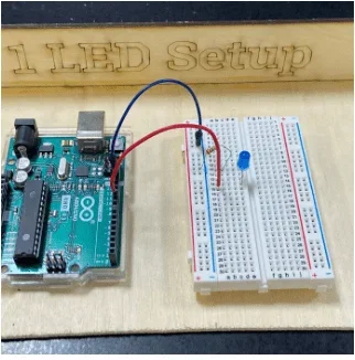 Photo showing a breadboard with a blue LED, resistor, and Arduino wired in series.