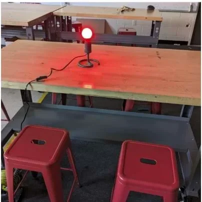 A photo showing a lamp without a cover with a red bulb turned on at the center of a desk.