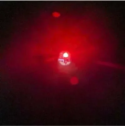 An image through a circular black tube lens of a lit red light bulb, which is clear and slightly magnified.