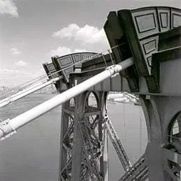 Photo shows close-up of cables at top of a bridge tower.