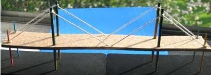 Photo shows a long bridge with two support towers in the middle region and cables between end and middle points and the tops of the towers.