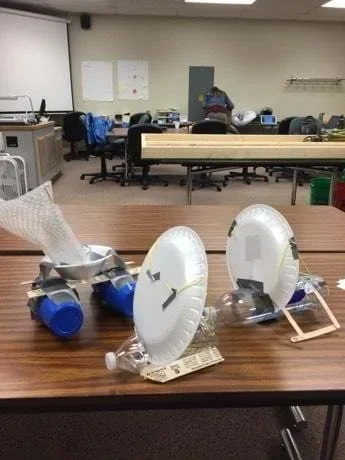 Three examples of final student boat designs sit on a classroom table.