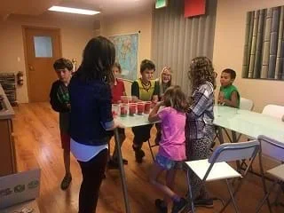 A picture of 5 students standing around a table with 4 cups filled with pom poms on the table.
