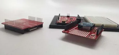 A photograph shows an Arduino microcontroller with an attached breadboard. Next to the Arduino are two SparkFun shields with soldered header pins.