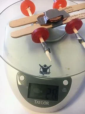 A mint-mobile sits on a small digital scale. Some pennies are taped to the top of the car; the scale reads 28 g.
