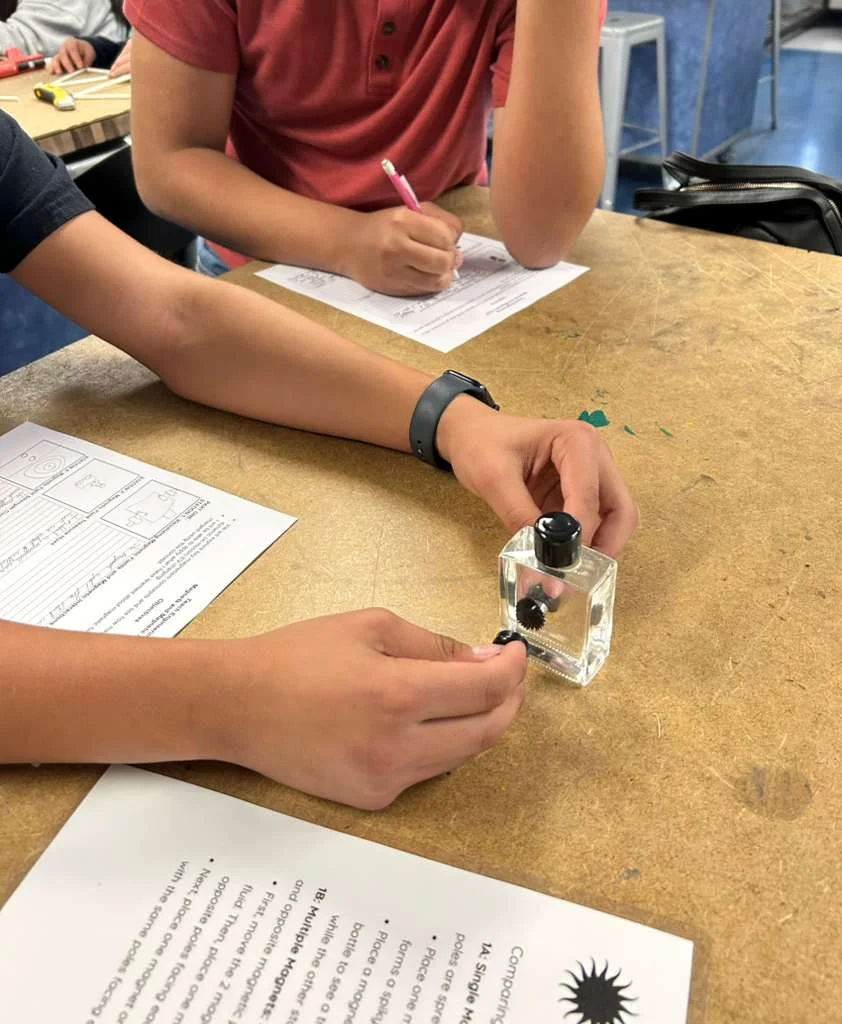A photo showing a ferrofluid bottle with a student placing a magnet on the either side of the bottle to visualize magnetic fields.