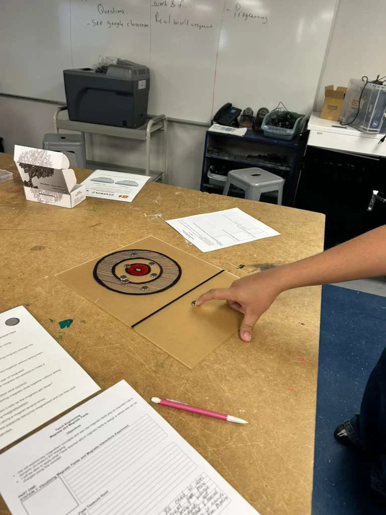 A photo showing a student using a round magnet to repel another smaller round magnet via the force of same magnetic polarity repulsion.
