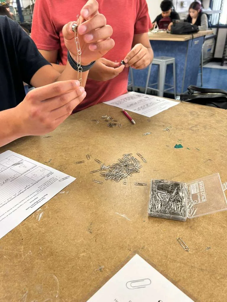 A photo showing a student using magnets to magnetically attract a string of paper clips end to end.