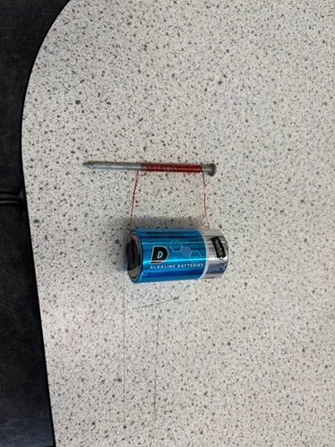 A photo showing an electromagnet made with a D-cell battery and a nail wrapped with insulated wire.