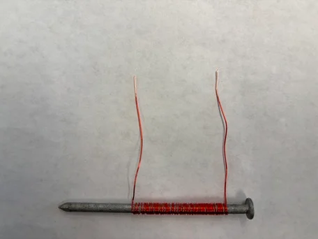 A photo showing a 4” uncoated steel nail wrapped with consecutive coils of thin insulated copper wire with ½” of the wire coating sanded off.