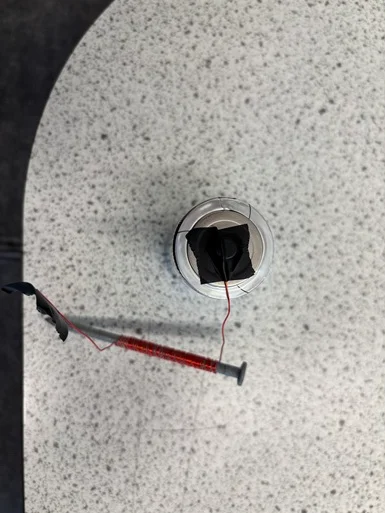 A photo showing a D-cell battery with one end of the wire lead of the wire-wrapped nail attached with electrical tape to a battery lead.