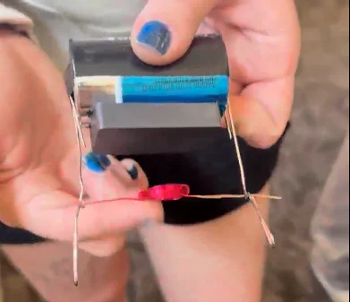A photo of a coil made of thin insulated copper wire with one end of the wire coating completely sanded off and the other end of the wire with half of the coating sanded off.