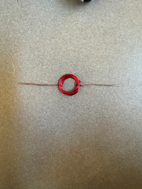 A photo of a coil made of thin insulated copper wire with one end of the wire coating completely sanded off and the other end of the wire with half of the coating sanded off.