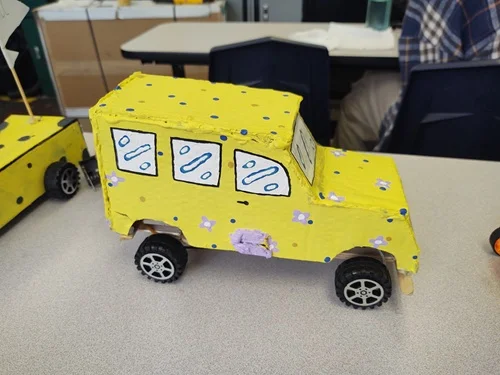 A photo of a model EV design that is decorated as a mini-yellow school bus with flowers.