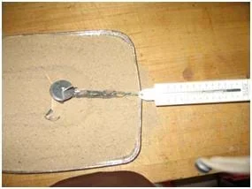 Photo from above the activity set-up shows a pan of sand on a table with a popsicle-stick device connected to a spring scale as it is pulled across the pan.
