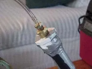 A photograph of clear plastic tubing run into metal fittings that cap the end of a vacuum cleaner hose. Duct tape provides additional sealing.