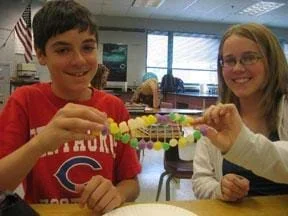 Photo shows two students holding a twisted ladder-like creation made of gumdrops and toothpicks.
