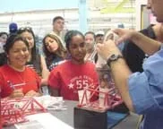 Students crowd around a model bridge, watching as weights are added to test its strength.