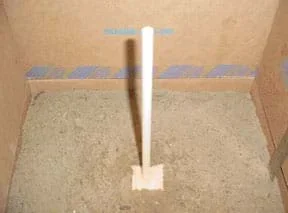 Photo shows the block of wood at the end of a dowel partially submerged in the top soil layer in a cardboard box.