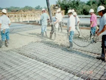 Photo shows men in construction hats and rubber boots walking on a metal grid.