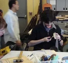 Photo shows a student at a classroom workbench attaching the heel to a shoe.