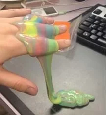 A photograph shows a hand with multi-colored silly putty dripping off it.