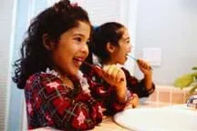 Photo shows two young girls brushing their teeth over a sink.