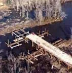 A photograph shows a wooden bridge in construction over a stream.