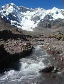 Photograph of a large mountain covered in snow (glacier) with a glacial stream flowing down valley of the mountain.