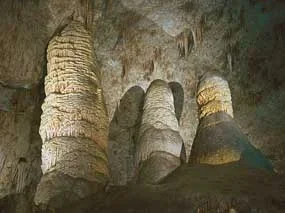 Photograph shows inside of a white stone cave with formations piled up from the floor and hanging down from the ceiling.