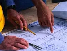 A photograph shows hands, pencil and compass on a laid-out blueprint drawing.