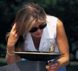 A picture of a woman drinking water from a fountain.