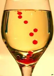 Round, red droplets are suspended in amber liquid in a wine glass.