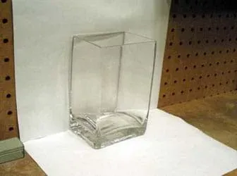 Photo shows two pieces of white paper affixed to a wall and a table top to form a white background for the glass container.