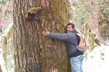 Photo shows a man hugging a big tree trunk.