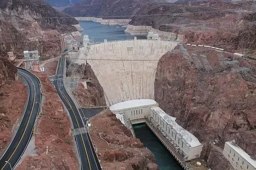 A photograph looking upstream at the dam, a narrow point in a steep canyon filled with a concrete structure, holding back the river.