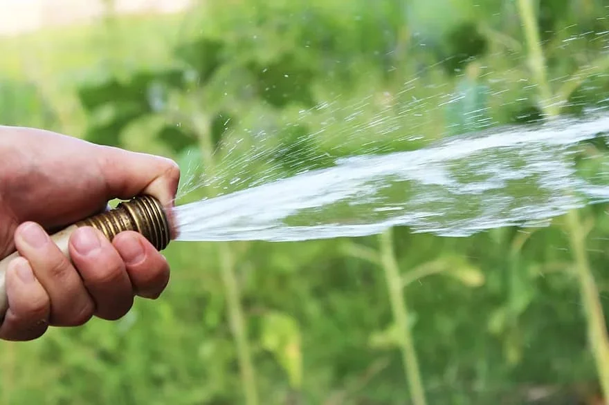 A photograph shows a person holding their thumb over a hose causing the water to spray out.