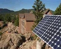 Photo shows a panel of solar cells on a rocky hillside near a home.