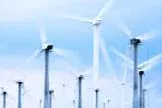 Photo shows the tops of about 20 giant three-blade wind turbine spinning against a blue sky.