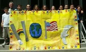Photograph of 10 kids holding a large banner with the word HOPE spelled out with images of the twin towers, rainbow, globe, flag and dove.