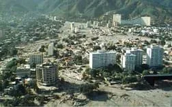 Aerial photo showing sediment poured around roads, buildings and skyscrapers in a valley and alluvial fan below mountains.