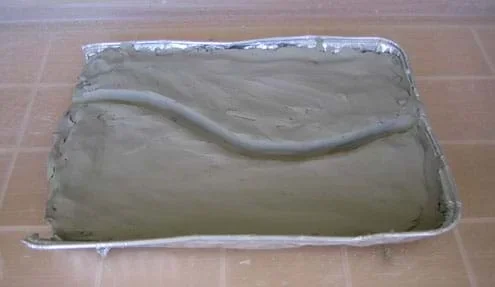 Baking pan filled with clay shaped into a slightly curved riverbed.