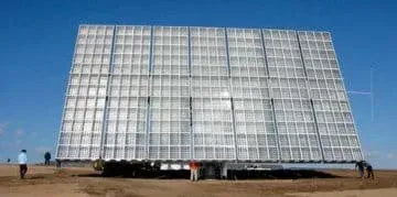 Photo shows a huge panel propped up and facing the sun in an open field. Panel is made of white and clear plastic in sliver metal grids. Panel looks very large next to the men standing near it—maybe 15 meters wide x 12 meters tall.