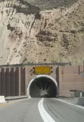 Photo shows view from a highway looking into an arched tunnel entrance cut into the rock face of a mountain.