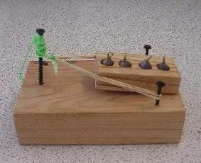 A photograph shows a completed model car body. The rubber band is pulled back and tied to the screw at the front of the vehicle. The weighted block is placed between the two screws at the back so that once the string is cut, the block will be propelled backwards.