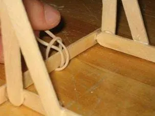 A photograph of the tying of the the rubber band around the base of the catapult.