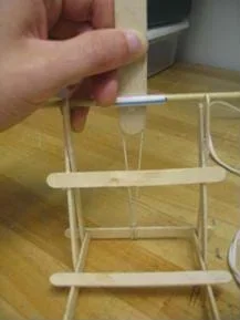 A photograph of Securing the tongue depressor to the wooden dowel/straw.