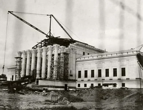 Photograph of a crane lifting materials onto a building under construction.