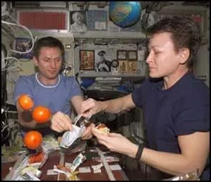 Photo shows a man and a woman holding food and using utensils as three oranges float nearby.