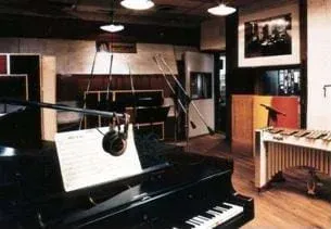 Photo shows a room with a piano, instruments and microphones  in the foreground along with other musical instruments.